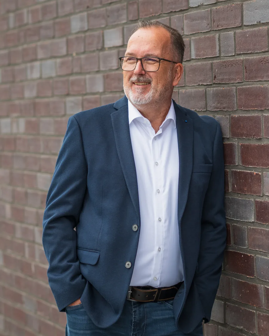 Björn-Olaf Lange in a jacket, smiling and leaning against a brick wall